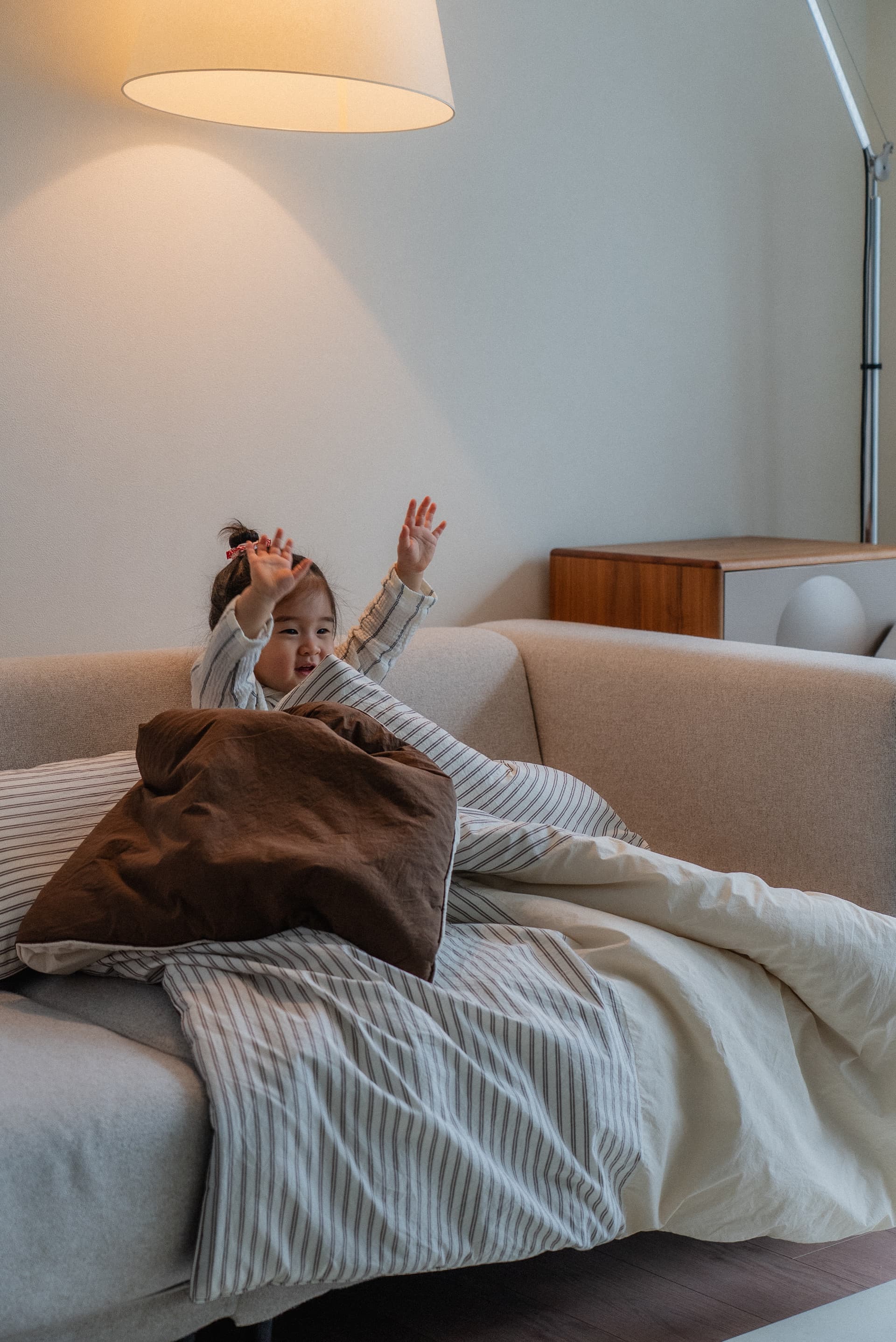 Toddler waving behind a cozy striped blanket